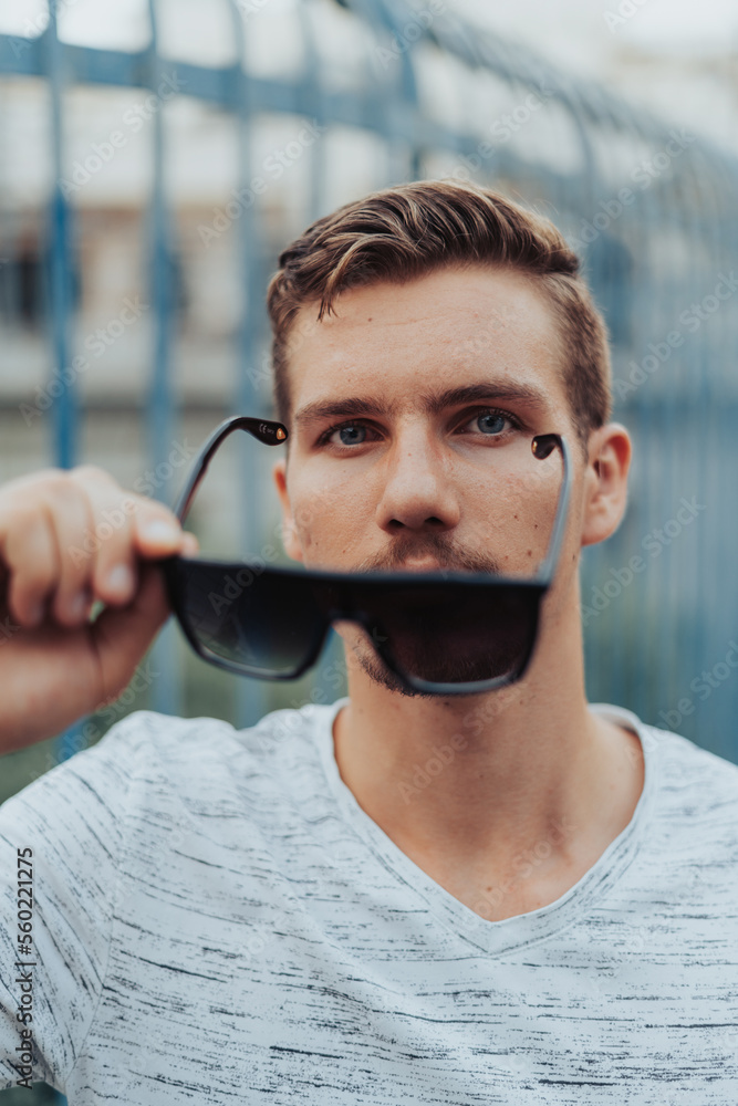 Portrait of Young Man Taking Off His Sunglasses, Looking into The Camera Portrait of Young Man Taking Off His Sunglasses, Looking into The Camera