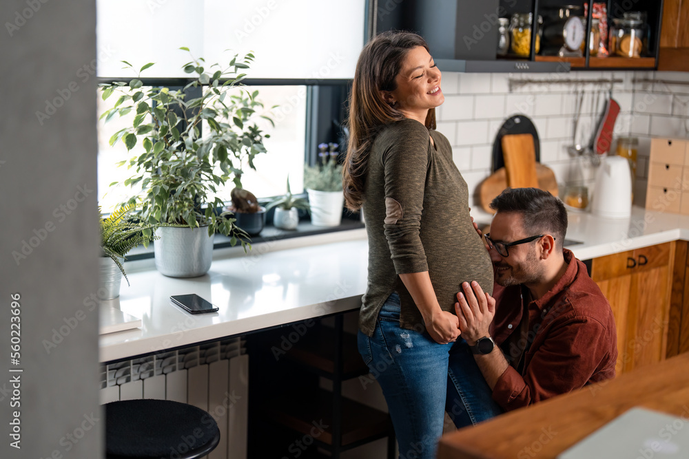 Handsome man wearing glasses is cuddling his wife's belly with love. Joyful pregnant woman enjoying the support and love of her husband. Handsome man wearing glasses is cuddling his wife's belly with love. Joyful pregnant woman enjoying the support and love of her husband.
