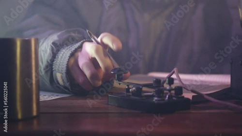 Man writes information in diary tapping finger on telegraph in dark room. Author communicates in Morse code sitting near mug with steam closeup photo