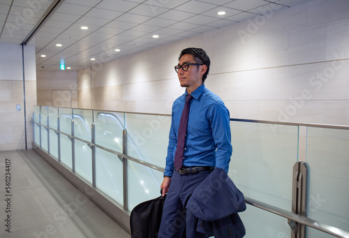 A young businessman in the city, on the move, a man standing on a walkway carrying a suit carrier and a hacket. photo