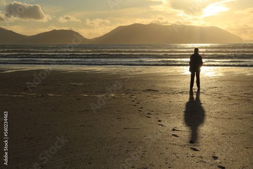 Silhouette of a person standing with their shadow behind them on the beach looking towards the mountains of Western Ireland at sunset with copy space (Inch Beach, Kerry, Ireland) Thoughtful background