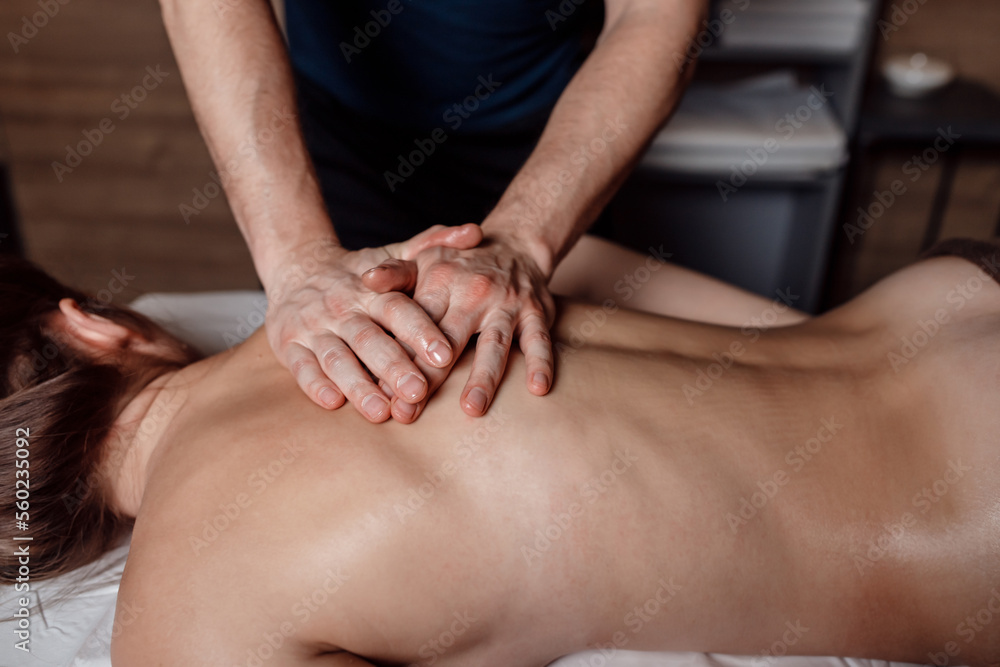 Male masseur doing back massage to client woman in dark room of massage spa Male masseur doing back massage to client woman in dark room of massage spa
