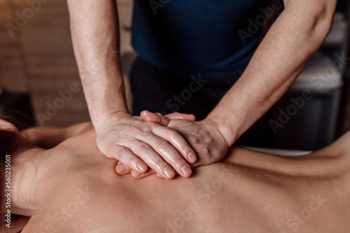 Male masseur doing back massage to client woman in dark room of massage spa