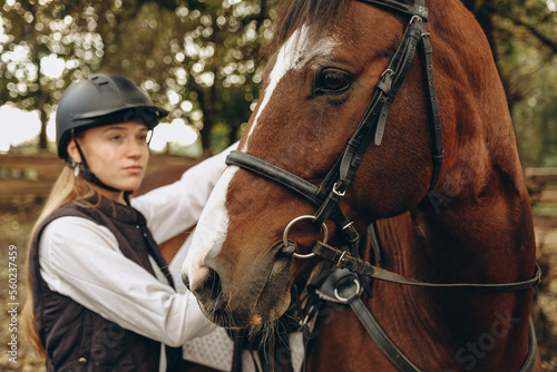 A young woman jockey adjusts the harness on her horse before training.