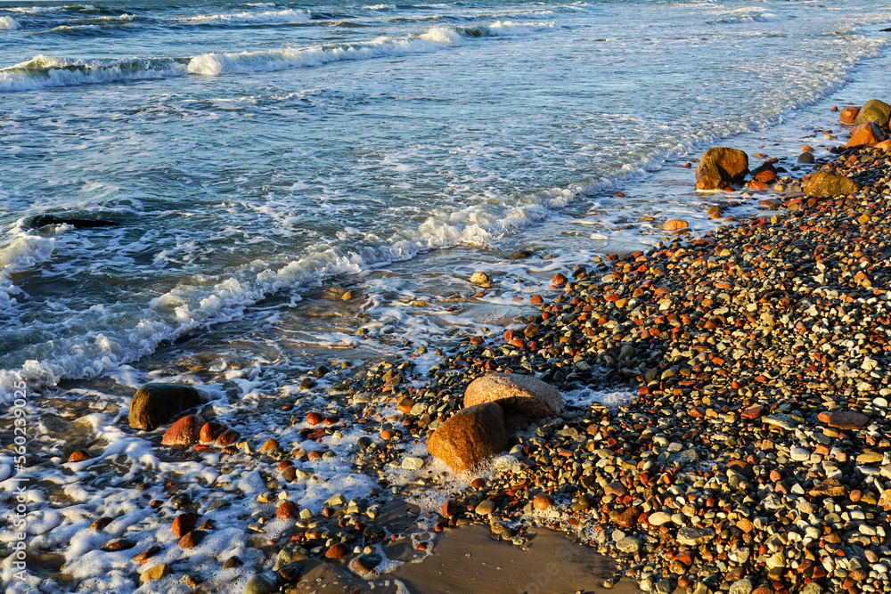 Beautiful view of rocky Baltic Sea coast, sand dune and waves with white foam tops in sunset light