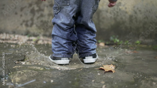 Child jumping into water puddle. Toddler wearing boots splash into puddle4
