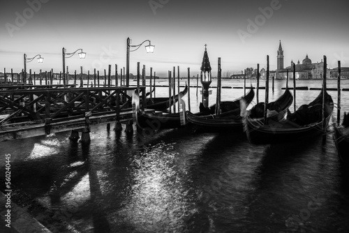 Long exposure: Gondolas floating by the shoreline of San Marco Square at sunrise in front of the Island of San Giorgio Maggiore in Venice, Italy in black and white