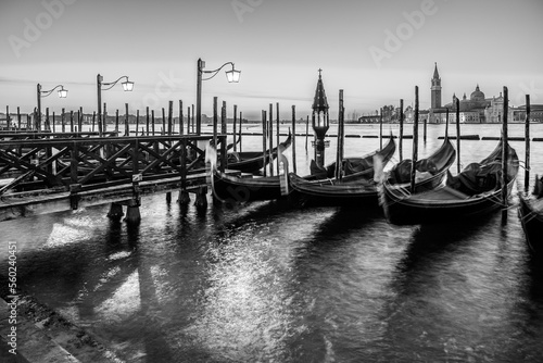 Long exposure: Gondolas floating by the shoreline of San Marco Square at sunrise in front of the Island of San Giorgio Maggiore in Venice, Italy in black and white