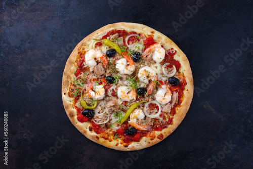 Traditionelle italienische Pizza frutti di mare Riesengarnelen, Tunfisch und Oliven serviert als Draufsicht auf einem rustikalen schwarzen Board 