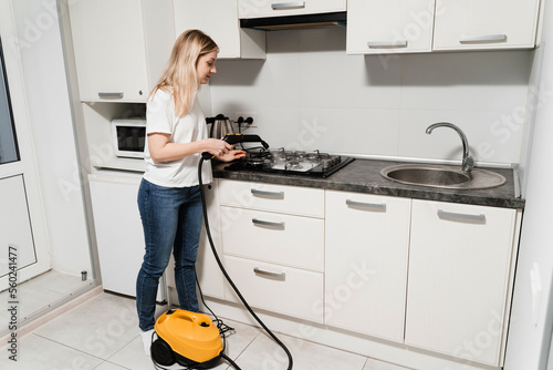 Steam cleaning of kitchen using professional steam generator. Woman cleaner is steaming and disinfecting cooker in kitchen. Girl worker of domestic cleaning service clean using vapour machine.