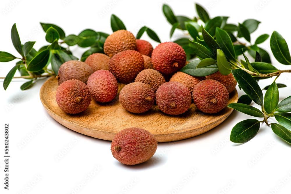 Litchi lie on a wooden plate, around a sprig with leaves, isolated Litchi lie on a wooden plate, around a sprig with leaves, isolated