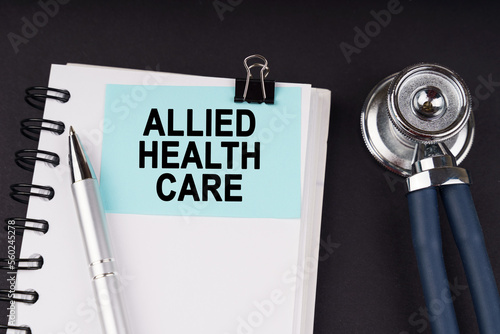On a black surface, a stethoscope, a notebook, a pen and a blue sticker with the inscription - Allied Health Care