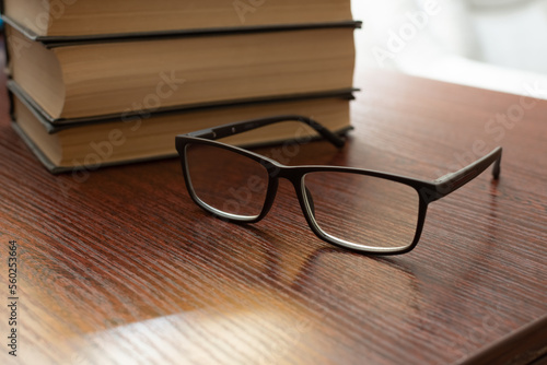 Stylish eyeglasses on office table close-up on blurred background of stack of books