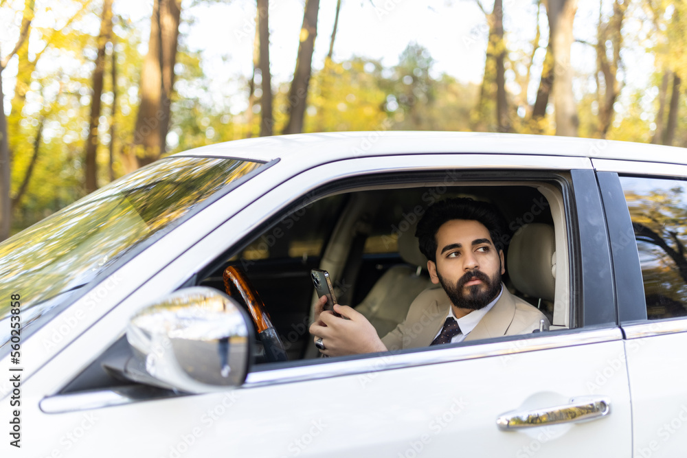 Cheerful arab man entrepreneur going to office by auto, using cellphone while driving car, chatting with someone, side view, copy space Cheerful arab man entrepreneur going to office by auto, using cellphone while driving car, chatting with someone, side view, copy space