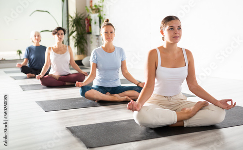 Relaxed young European female sitting in meditation Lotus Pose Padmasana during yoga class with other women