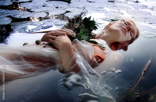 Gorgeous beautiful portrait of a young sexy woman Ophelia with curly red hair lying peaceful, quiet, calm with flowers and eyes closed dying in the water