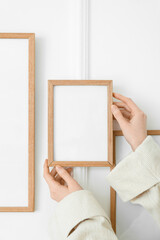 Woman hanging blank photo frame on light wall, closeup