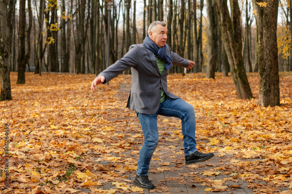 Full length photo of energetic aged man dancing on path in golden forest. Fallen dry yellow maple leaves everywhere. Full length photo of energetic aged man dancing on path in golden forest. Fallen dry yellow maple leaves everywhere.