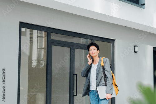 Young successful woman in jacket with computer on background of office buildings