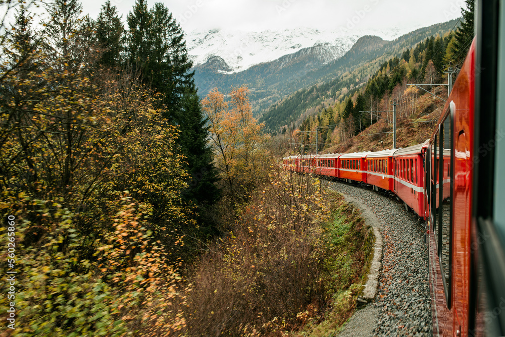 Tourist red Swiss train rides through the autumn Alps. Autumn in the mountains