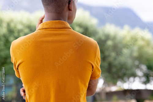 Image of rear view of biracial man in orange short sleeve polo t shirt with copyspace