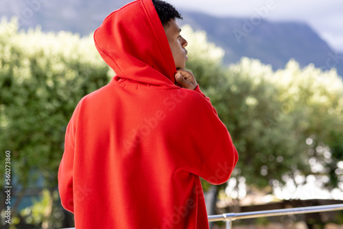 Image of biracial man in red hooded top with copyspace over trees in background