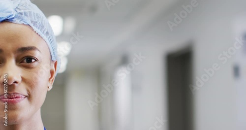 Video half face portrait of smiling biracial female medical worker in cap, in corridor, copy space photo