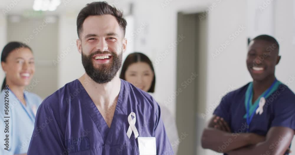 Video portrait of happy caucasian male doctor with cancer ribbon in hospital corridor, copy space Video portrait of happy caucasian male doctor with cancer ribbon in hospital corridor, copy space
