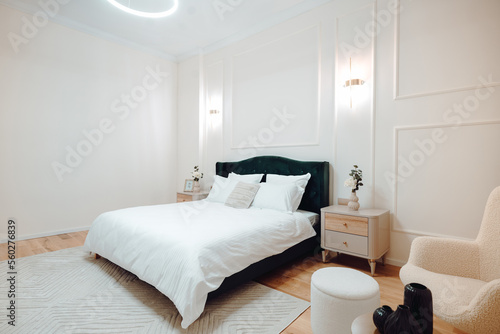 Bedroom and interior design with canvas over bed with linens, beige walls, nightstand and carpet