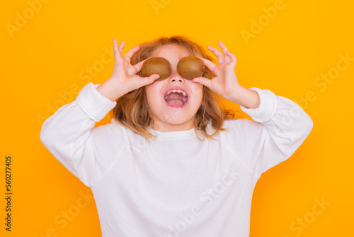 Child hold kiwi in studio. Kiwi fruit. Studio portrait of cute kid boy with kiwi isolated on yellow.