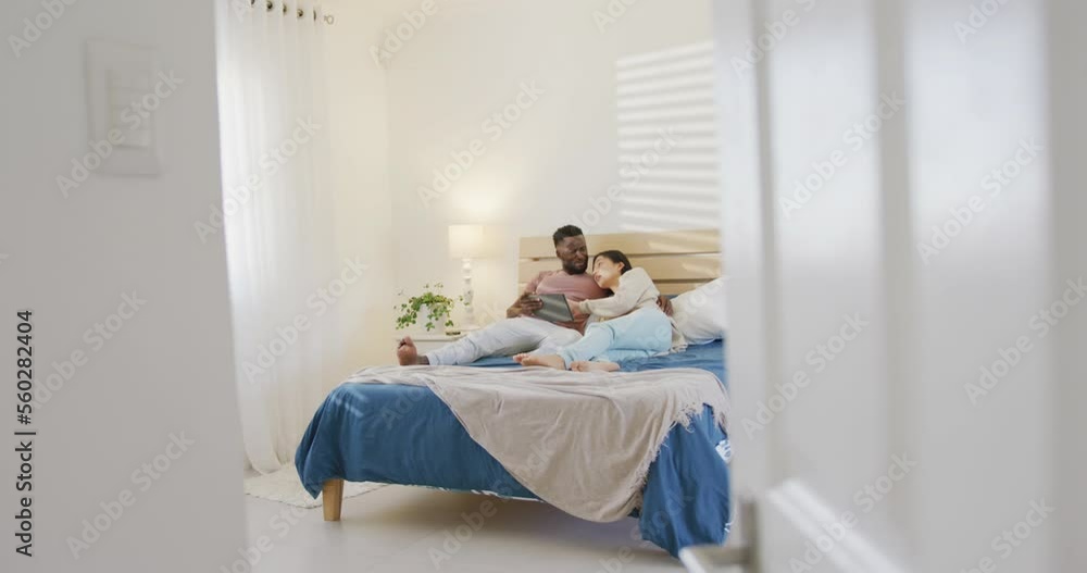 Happy diverse couple using tablet and lying in bedroom Happy diverse couple using tablet and lying in bedroom