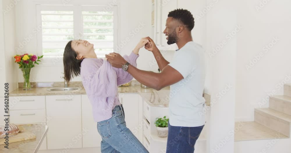 Happy diverse couple holding hands and dancing in kitchen