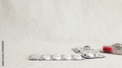 Used medicine blister pack with white and red pills falling from top frame and piling up on white background in a normal view and a ground level