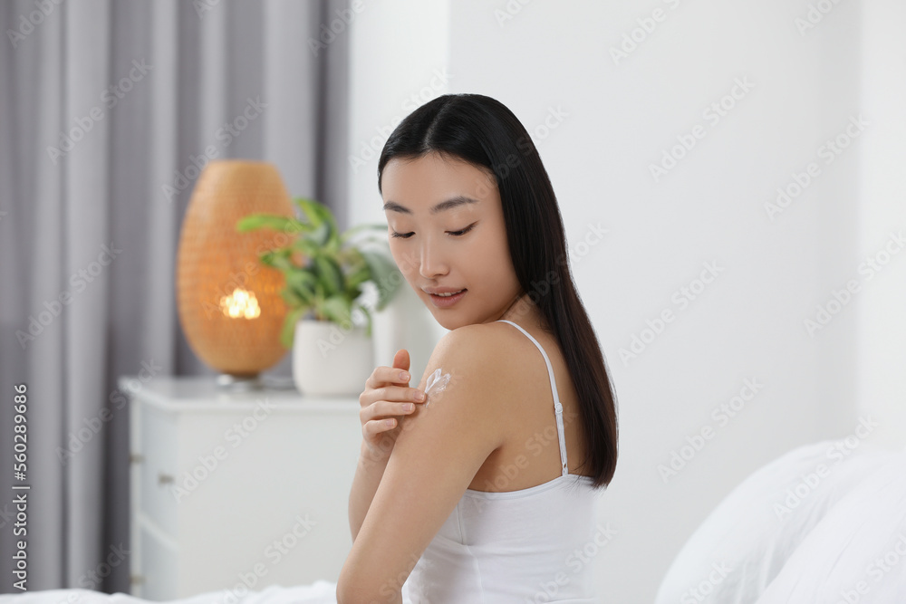 Beautiful young Asian woman applying body cream on shoulder in bedroom Beautiful young Asian woman applying body cream on shoulder in bedroom