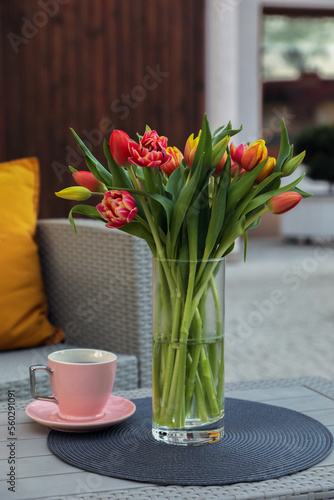 Beautiful bouquet of colorful tulips and cup with drink on rattan garden table outdoors