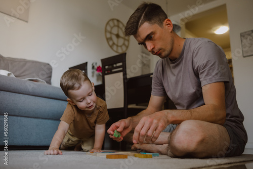 dad and son assemble a wooden puzzle on the floor of the house