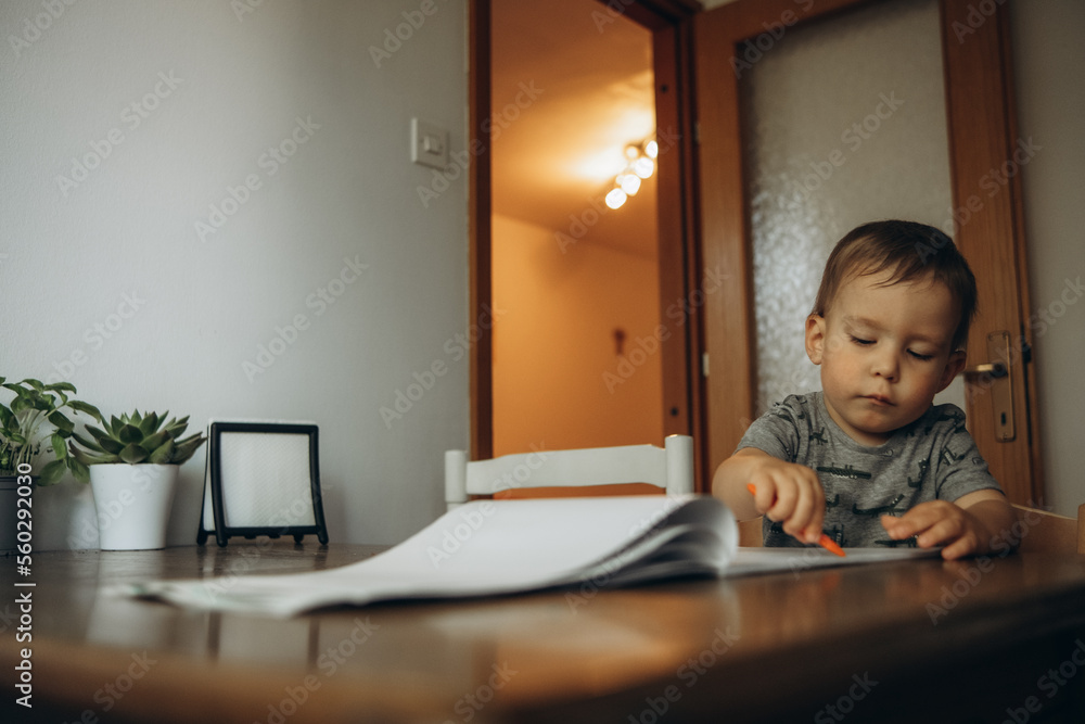 a child draws with colored pencils at a table on a white sheet of paper a child draws with colored pencils at a table on a white sheet of paper
