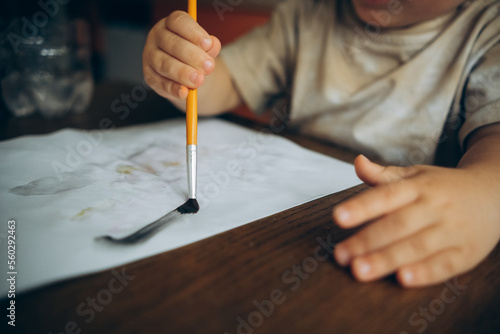 the child draws with a brush and paints on a white sheet of the album..detail. the hand holds the brush