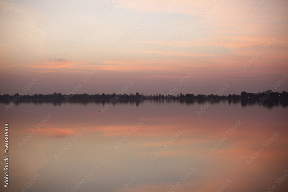 Scenic view of beautiful sunrise or dawn above the pond at spring or early summer morning with cloudy sky background and fog over water. Landscape. Water reflection.