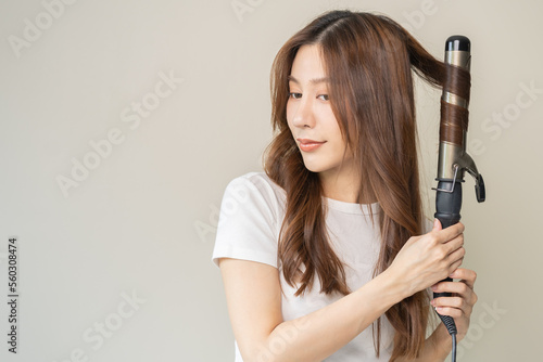 Canvas Print Beautiful curly brunette, attractive asian young woman, girl smiling using curler, curling iron long hair with ceramic curler straightener at home