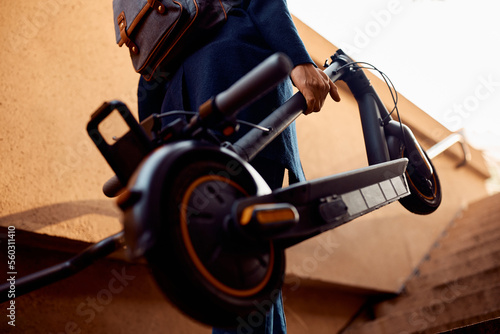 Close up of man carrying electric scooter while walking upstairs outdoors.