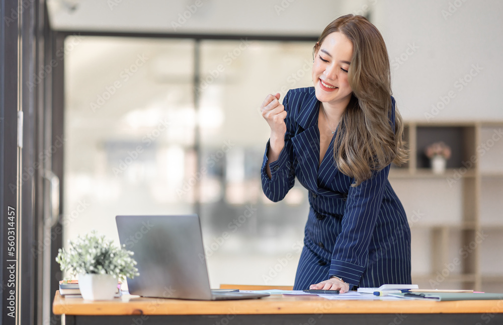Happy excited Asian Woman holding laptop and raising his arm up to celebrate success or achievement in the workplace office Happy excited Asian Woman holding laptop and raising his arm up to celebrate success or achievement in the workplace office