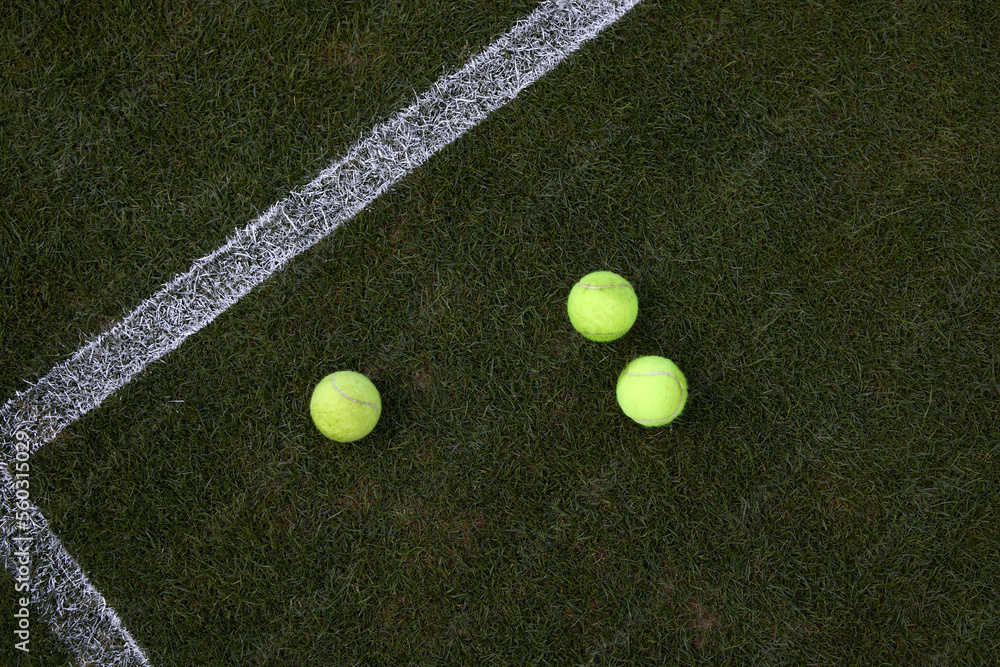 Tennis balls next to a white line on a grass court