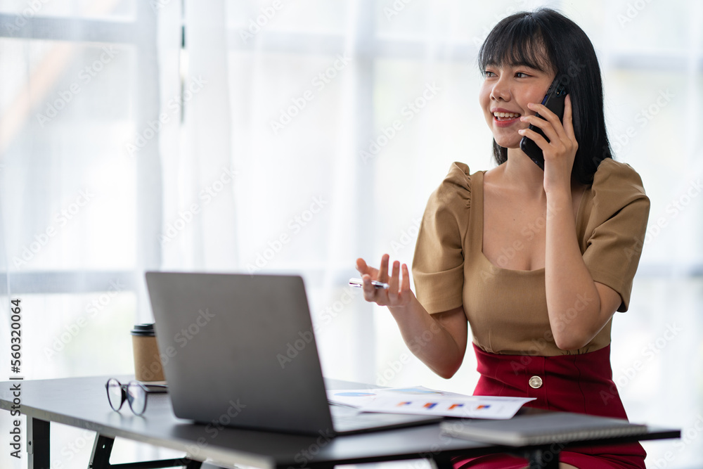Happy young asian woman talking on the mobile phone and smiling while sitting at her working place in office. Happy young asian woman talking on the mobile phone and smiling while sitting at her working place in office.