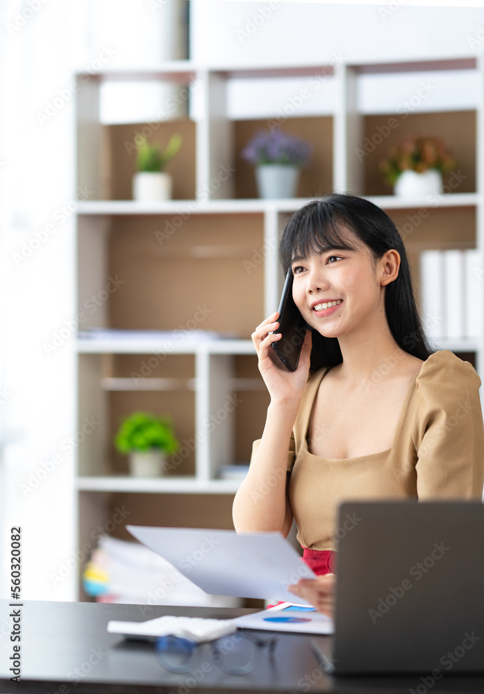 © crizzystudio - Happy young asian woman talking on the mobile phone and smiling while sitting at her working place in office.