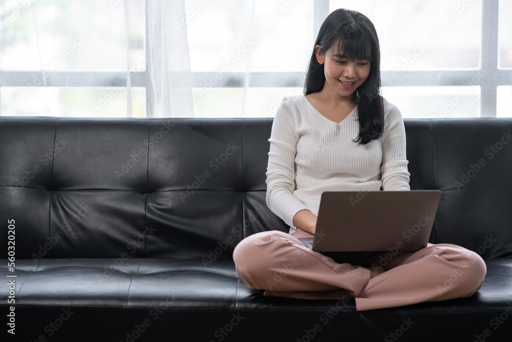 Asian woman using laptop to work at home, sitting on sofa Asian woman using laptop to work at home, sitting on sofa