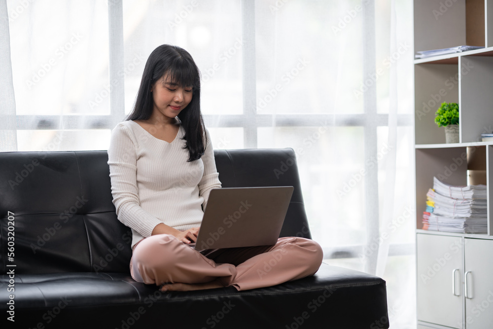 Asian woman using laptop to work at home, sitting on sofa Asian woman using laptop to work at home, sitting on sofa