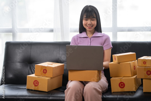 Asian women working SME business at the workplace at home. use laptop to check customer orders online shipping boxes, freelance SME entrepreneur online business idea.