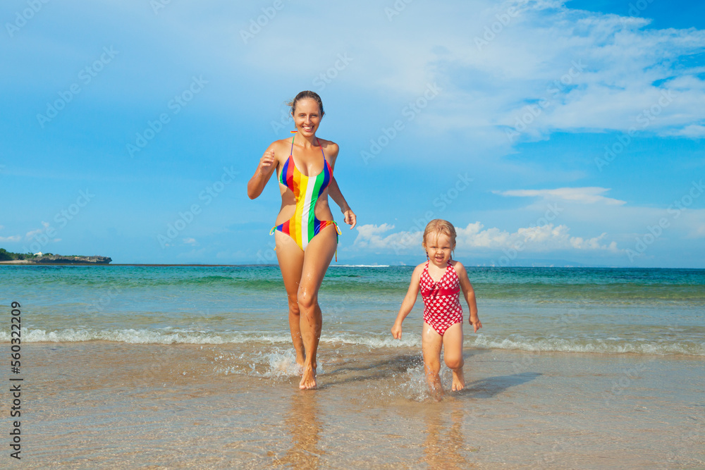 Happy kid with mother have fun on sea sand beach. Child with mother run by sea surf. Travel lifestyle, swimming activities in family summer camp. Vacations on tropical island.