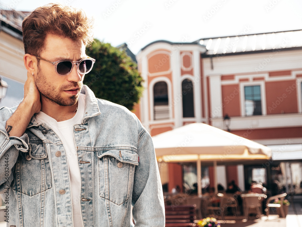 Portrait of handsome confident stylish hipster model. Sexy man dressed in jeans jacket. Fashion male posing in the street. In sunglasses in Europe city. Outdoors at sunset Portrait of handsome confident stylish hipster model. Sexy man dressed in jeans jacket. Fashion male posing in the street. In sunglasses in Europe city. Outdoors at sunset